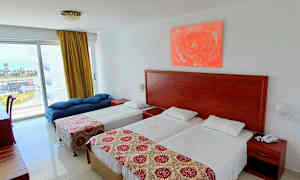 Ett hotellrum med två enkelsängar, en dagbädd och ett bord vid fönstret. (AI-genererad text)