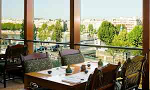 En restaurang med bord och stolar nära ett stort fönster med utsikt över staden och floden. (AI-genererad text)