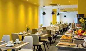Ett modernt restaurangområde med gula väggar, uppdukade bord och en buffé med olika livsmedel. (AI-genererad text)