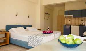 Rummet har en säng med blått sänggaveltäcke, ett kök och ett bord med frukt. (AI-genererad text)