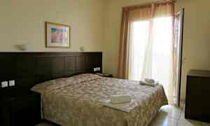 Ett hotellrum med en dubbelsäng, sängbord och en öppen balkongdörr. (AI-genererad text)