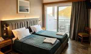 Hotellrum med två enkelsängar, sängbord och tavla på väggen. Balkong med utsikt över vatten och berg. (AI-genererad text)