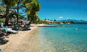 En strand med klart vatten, solstolar och träd. (AI-genererad text)