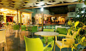 En utomhuslounge med bord och stolar intill en pool, belyst på kvällen. (AI-genererad text)