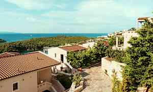 Utsikt över semesterbostäder med terrakottatak omgivna av grönska, och havet i bakgrunden. (AI-genererad text)