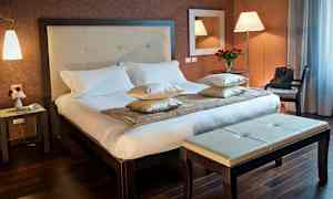 Ett hotellrum med en dubbelsäng, sidobord och bänk. (AI-genererad text)