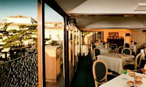 En restaurang med glasväggar och utsikt över byggnader och träd. (AI-genererad text)