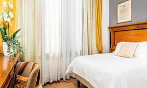 Ett hotellrum med en säng, ett skrivbord och en stol. Gardiner hänger vid ett fönster. (AI-genererad text)