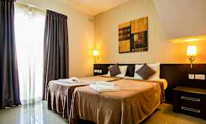 Ett hotellrum med två enkelsängar, sängbord, vägglampor, en målning ovanför sängarna och gardiner vid ett fönster. (AI-genererad text)