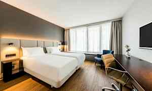 Ett ljust hotellrum med två enkelsängar, ett skrivbord, en tv och ett fönster med gardiner. (AI-genererad text)