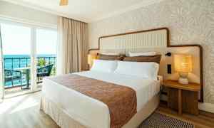 Ett hotellrum med en stor säng, två sängbord med lampor och en balkong med utsikt mot havet. (AI-genererad text)