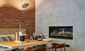 En mysig matplats med bord klätt i trä, bricka med tillbehör, två vinglas och öppen spis i bakgrunden. (AI-genererad text)