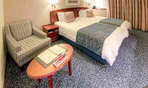 Ett hotellrum med två bäddade enkelsängar, en randig fåtölj och ett soffbord med broschyrer. (AI-genererad text)