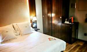 Ett hotellrum med en säng och upplyst nattlampa bredvid ett mörkt träskåp. (AI-genererad text)