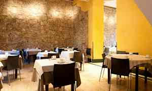 Ett rum med bord och stolar, vit duk och kaffekoppar samt stenväggar och gula väggdetaljer. (AI-genererad text)