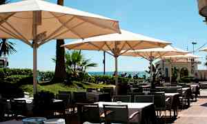 Resturangområde utomhus med bord, stolar och parasoller nära havet. (AI-genererad text)