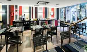 En matsal med flera bord och stolar, modern inredning och ett bufféområde längs bakre väggen. (AI-genererad text)