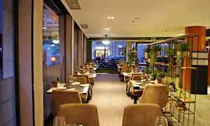 En mysig restaurang med bord och stolar arrangerade längs fönster och ett dekorativt ställ med växter. (AI-genererad text)