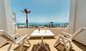 Terrass med två vita stolar och ett bord, två drycker och utsikt över stranden och havet. (AI-genererad text)