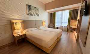 Ett hotellrum med två enkelsängar, nattduksbord, en arbetsyta och en fåtölj bredvid ett fönster. (AI-genererad text)
