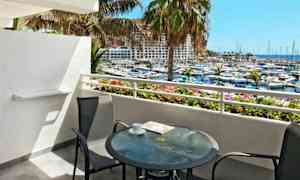 Utsikt från en balkong med ett glasbord och två stolar som vetter mot en marina och havet. (AI-genererad text)