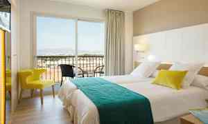 Ett hotellrum med två sängar, en stol och en balkong med utsikt. (AI-genererad text)