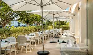 En utomhusterrass med vita bord och stolar samt vita parasoller. (AI-genererad text)