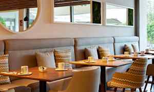 Ett modernt café med träbord, stolar och soffor. På borden står koppar och små skålar. (AI-genererad text)