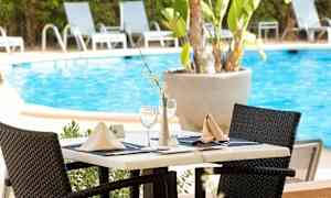 Ett dukat bord vid en pool, omgiven av solstolar. (AI-genererad text)