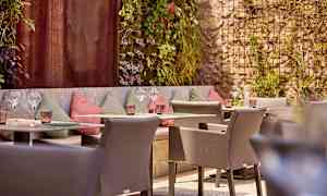 En uteservering med sittplatser och dekorerade väggar, omgiven av grönska. (AI-genererad text)
