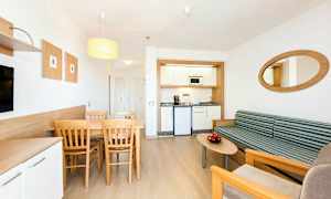 En modern hotellrum med ett litet köksutrymme, en matplats med bord och stolar samt en sittgrupp med soffa och soffbord. (AI-genererad text)