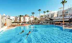 En stor utomhuspool framför vita byggnader och palmer. (AI-genererad text)