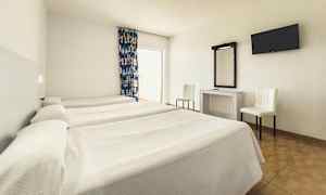 Ett hotellrum med tre enkelsängar, ett skrivbord med spegel, två stolar och en väggmonterad TV. (AI-genererad text)