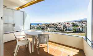 En balkong med bord och stolar som vetter mot en utsikt över staden och havet. (AI-genererad text)