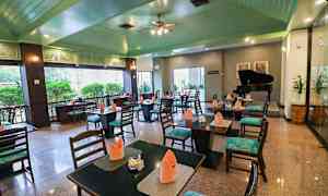 Interiör av en restaurang med bord och stolar, dukningar med orange servetter och en flygel i bakgrunden. (AI-genererad text)