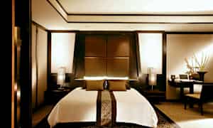 Ett modernt sovrum med en stor säng i mitten, omgiven av eleganta mörka träpaneler och varma ljuskällor. (AI-genererad text)