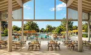 En restaurang med bordsuppställningar inomhus, med utsikt över en pool och trädgård genom stora fönster. (AI-genererad text)
