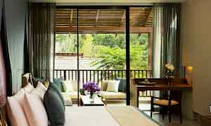 Ett hotellrum med en säng och en liten skrivbordsplats, samt en terrass med sittmöbler och utsikt över grönska. (AI-genererad text)