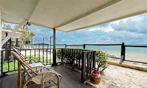 Utsikt från en terrass med rottingmöbler mot en sandstrand och havet. (AI-genererad text)