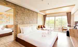 Ett rymligt hotellrum med en stor säng, sandstensvägg, spegel, soffa och fönster som leder till en balkong. (AI-genererad text)