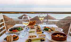 Ett dukat bord med olika maträtter och vinglas, med utsikt över stranden och havet. (AI-genererad text)