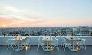 En takterrass med bord och stolar och utsikt över en stad vid solnedgång. (AI-genererad text)