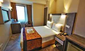 Ett hotellrum med en bäddad dubbelsäng. Det finns skrivbord, stol och fönster med gardiner. (AI-genererad text)