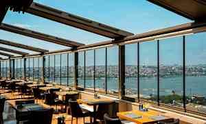 En restaurang med stora fönster som har utsikt mot en stad och ett vattendrag. (AI-genererad text)