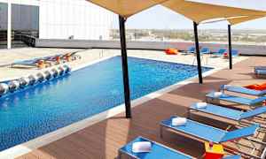 En modern pool med blått vatten omgiven av solstolar och skuggtält. (AI-genererad text)