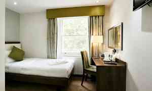 Hotellrum med en enkelsäng, fönster, skrivbord och stol. (AI-genererad text)