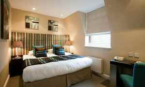 Ett hotellrum med en dubbelsäng med randig sänggavel och två sidobord med lampor. Ett skrivbord med stol vid ett fönster. (AI-genererad text)