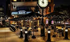 En uteservering vid en restaurang eller hotell med skyltning och klocka, kvällsbelysning. (AI-genererad text)