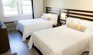 Ett hotellrum med två vita sängar och färgglada kuddar. (AI-genererad text)