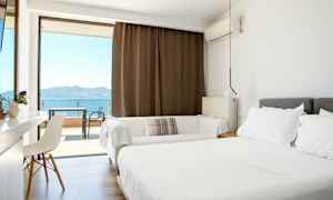 Ljust hotellrum med dubbelsäng och balkong med havsutsikt. (AI-genererad text)